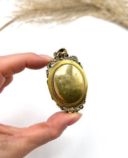 An ornate yellow gold oval locket pendant, held in a hand