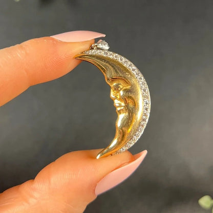 A gold crescent moon pendant with diamonds, held in a hand