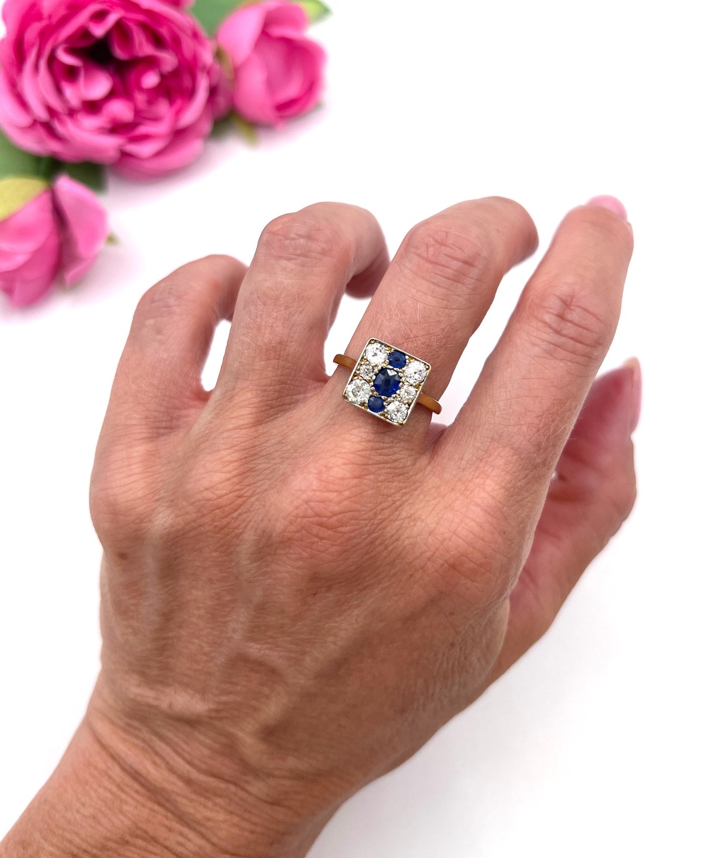 A square-shaped cluster ring with sapphires and diamonds in yellow gold and platinum, modelled on a hand