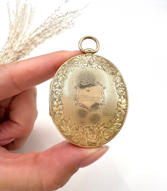 An oval yellow gold locket with intricate engraving, held in a hand