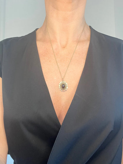 A cabochon garnet pendant with a seed pearl border in rose gold, with a chain, modelled by a woman
