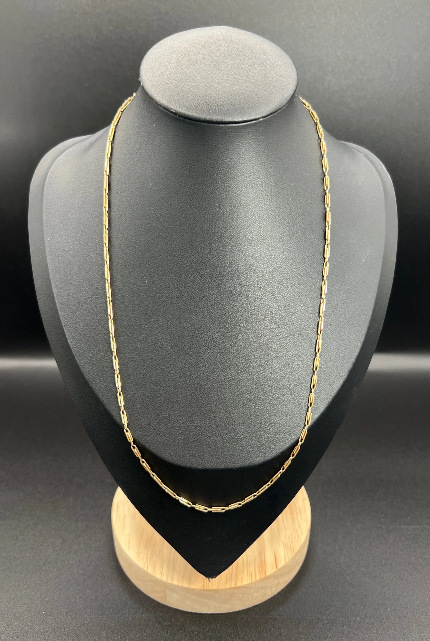 A gold paperclip link chain necklace, on a black bust