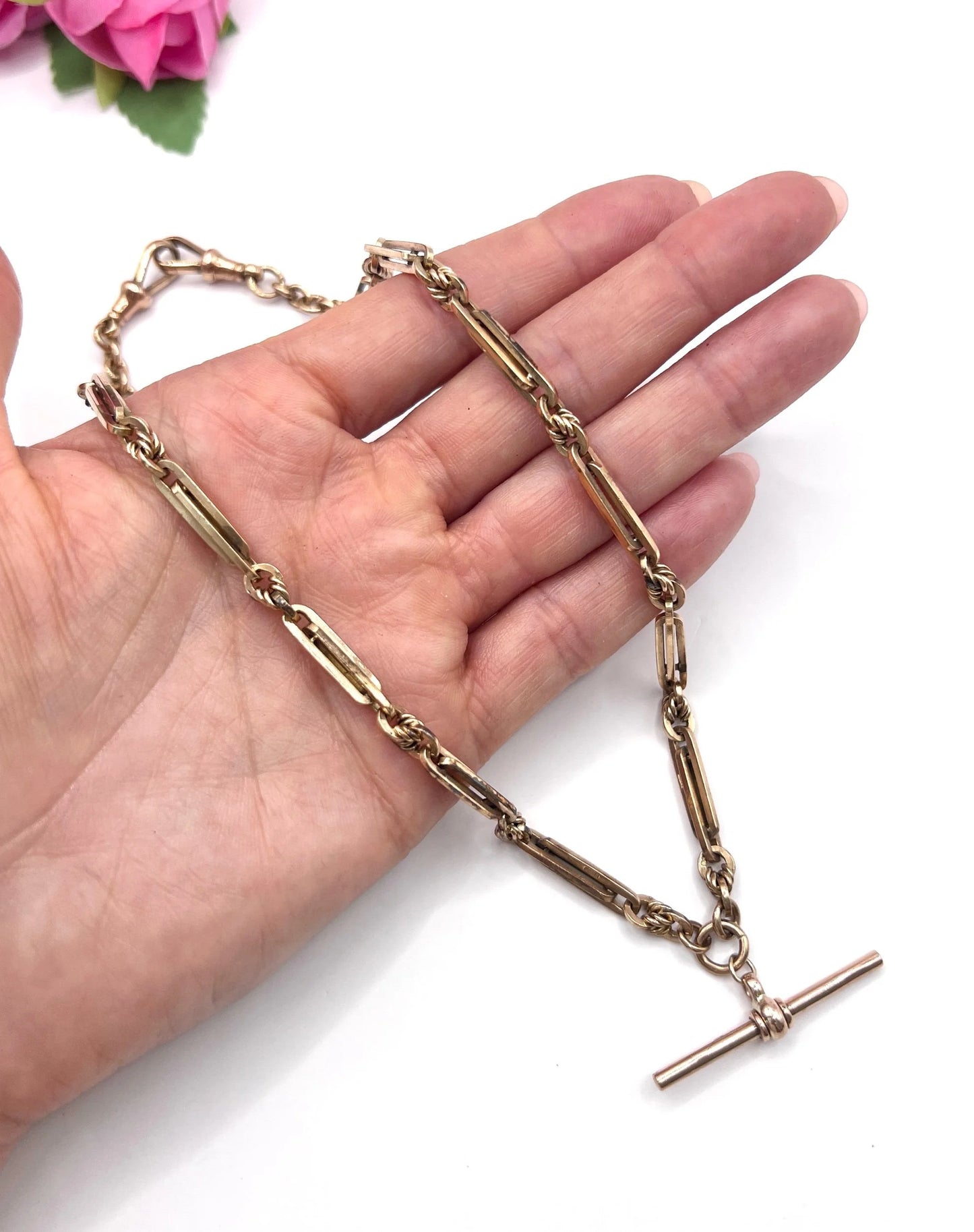 A rose gold fancy link Albert chain necklace, held in a hand