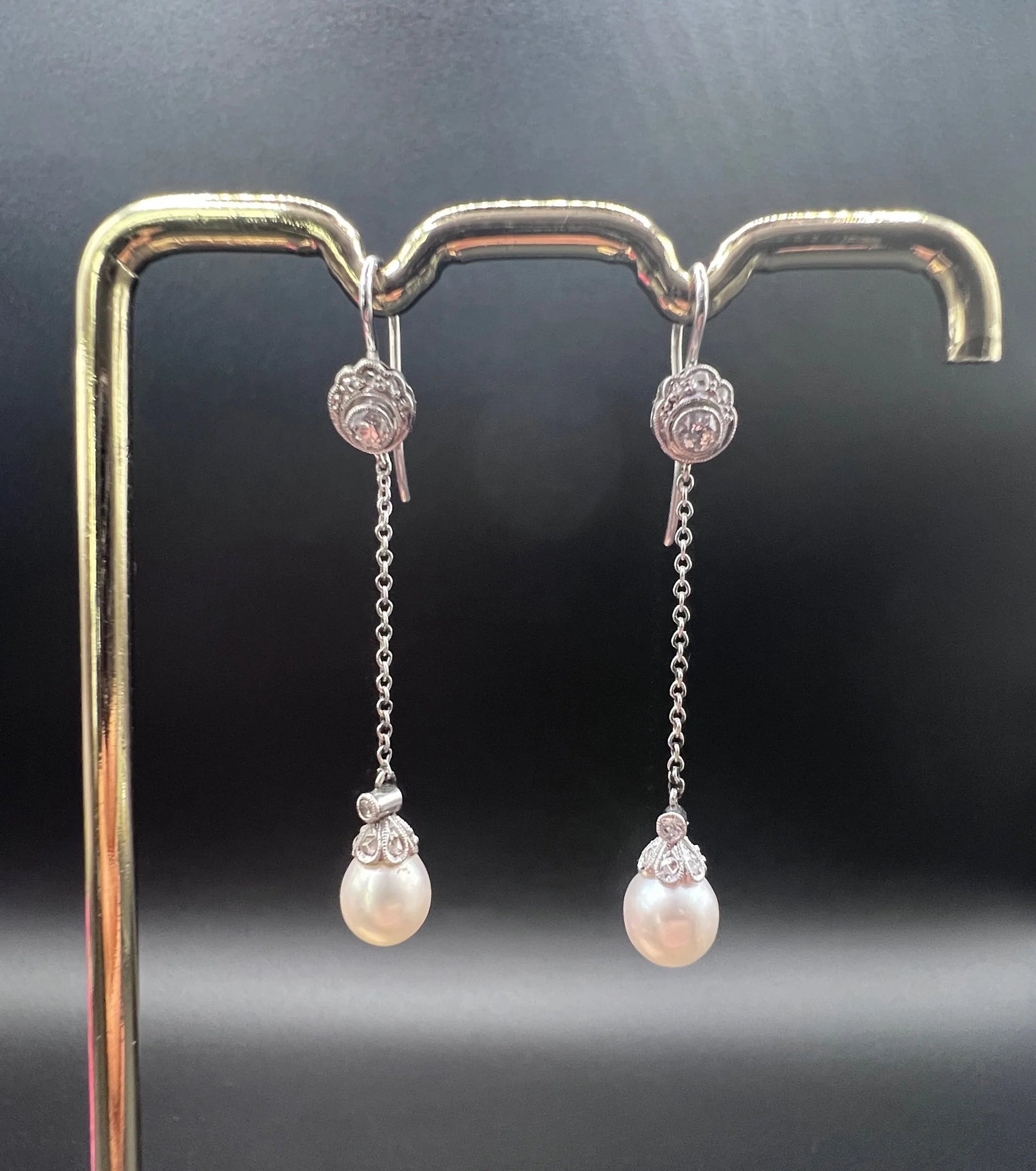 A pair of long drop platinum earrings with pearls and diamonds, on a gold hook