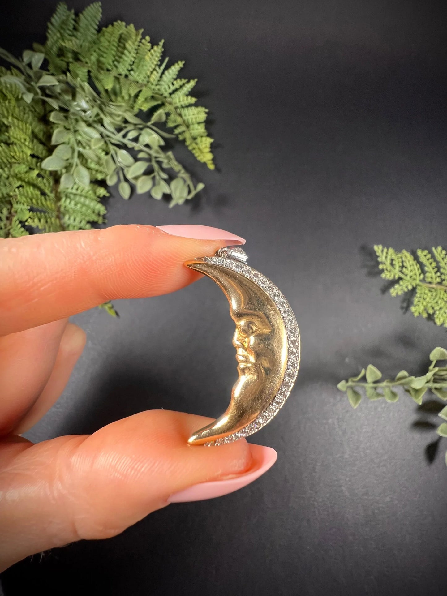 A gold crescent moon pendant with diamonds, held in a hand