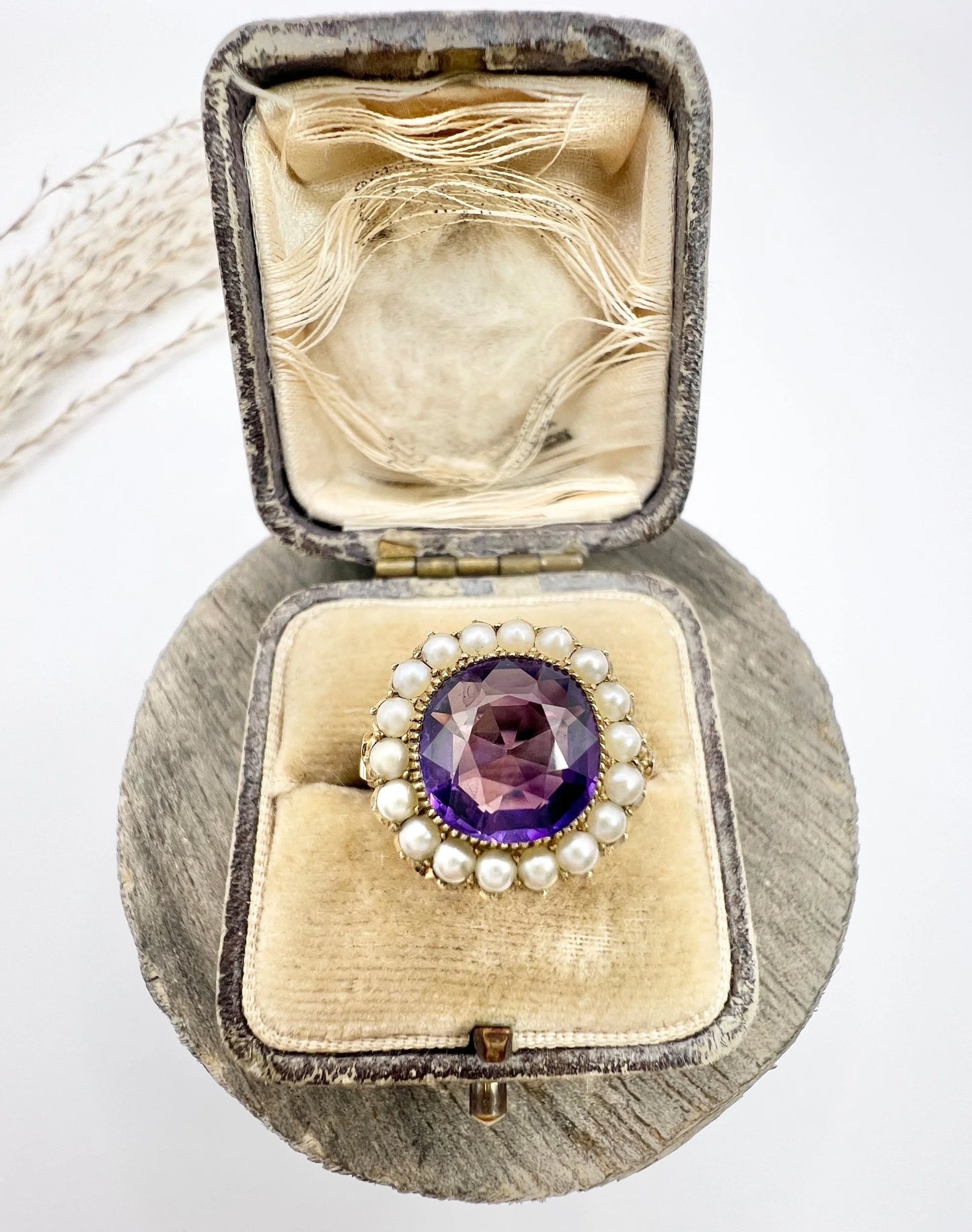 A cushion shaped amethyst cluster ring with a pearl border, in yellow gold, in a ring box