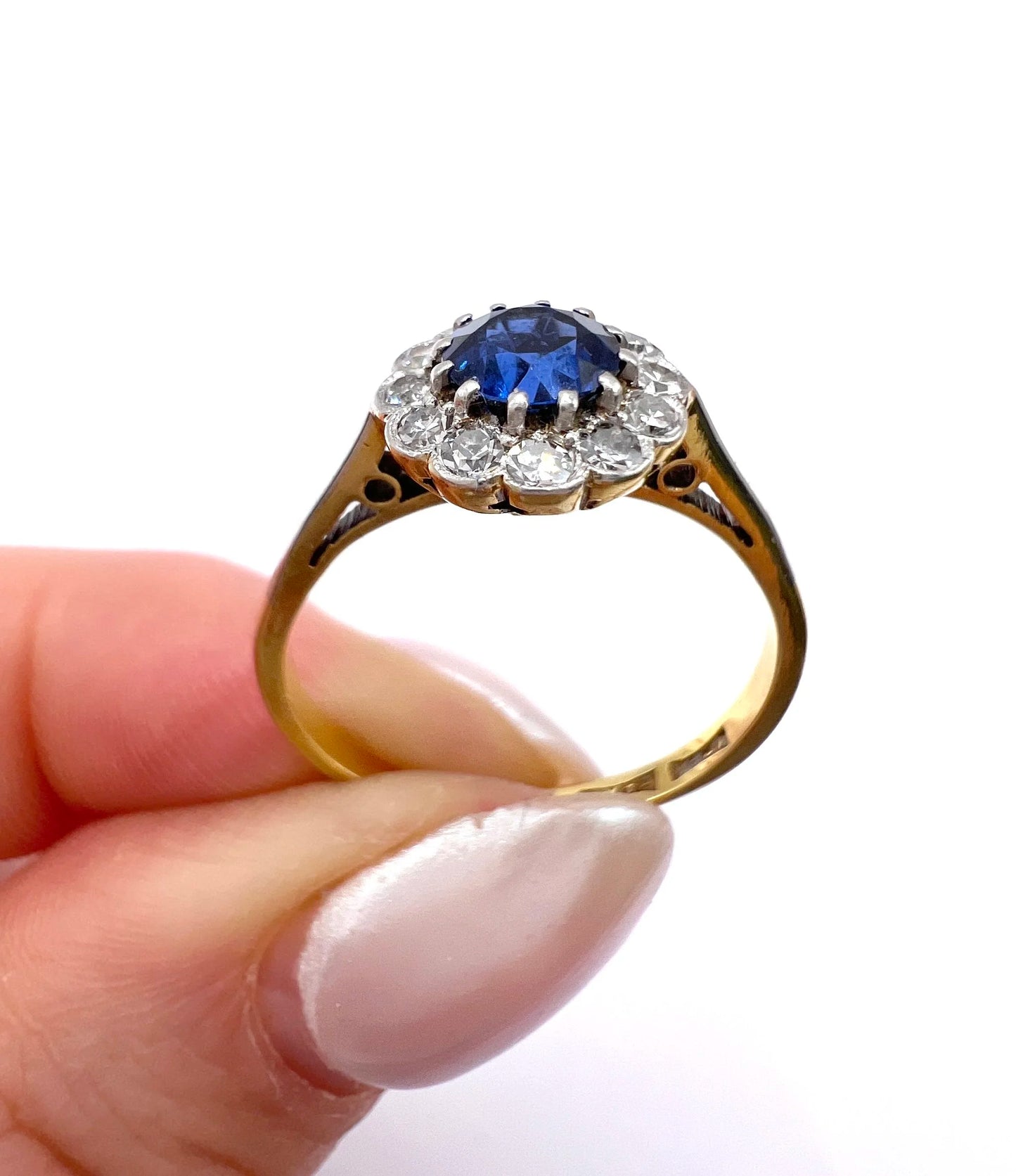 A sapphire and diamond flower cluster ring in yellow gold and platinum, held in a hand