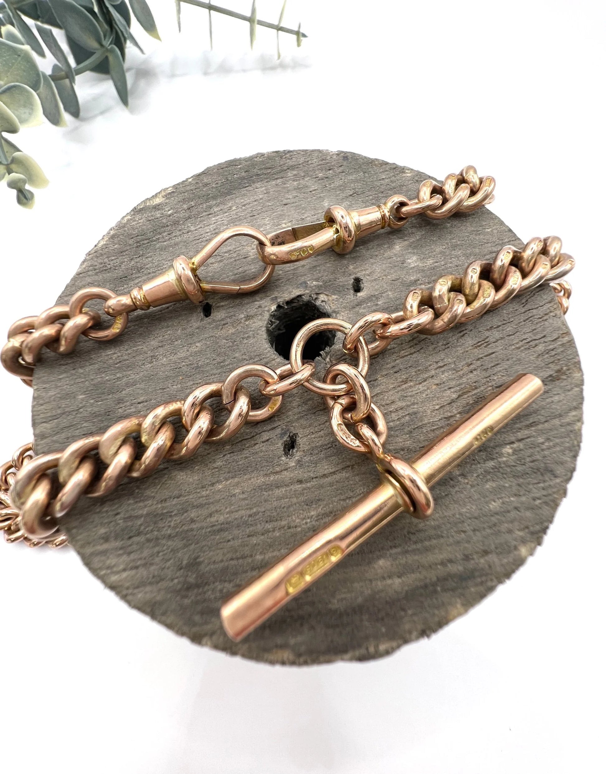 A rose gold curb link Albert chain on a wooden item against a white background