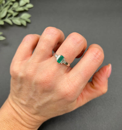 A five stone emerald cut emerald and baguette and square cut diamond ring in platinum, modelled on a hand