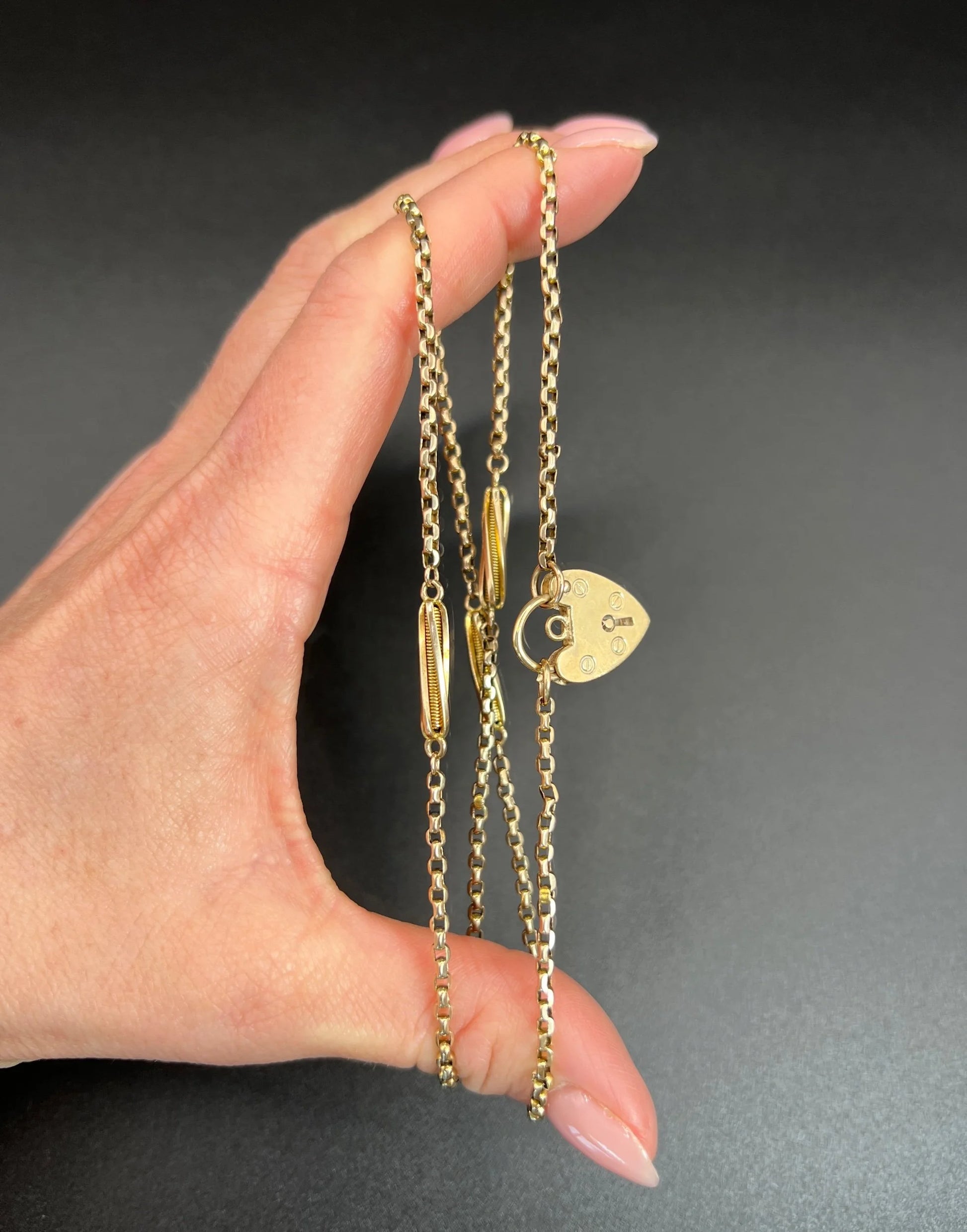A yellow gold fancy link chain with a heart padlock, held in a hand
