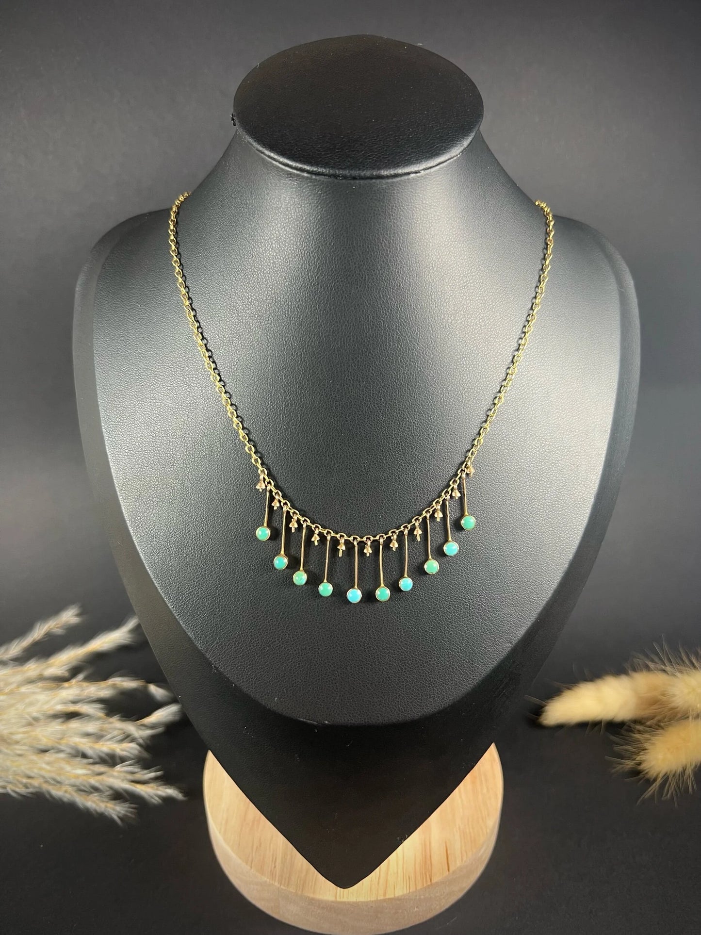 A gold negligee pendant necklace with turquoise drops, on a black bust