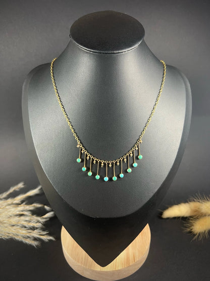 A gold negligee pendant necklace with turquoise drops, on a black bust