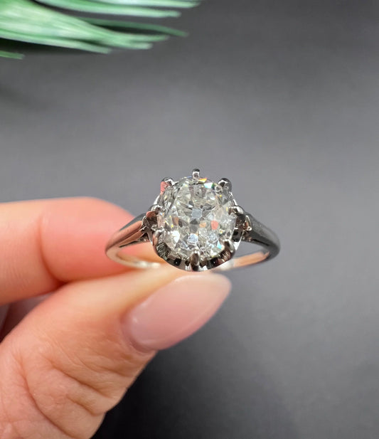 A white gold and platinum solitaire diamond ring, held in a hand