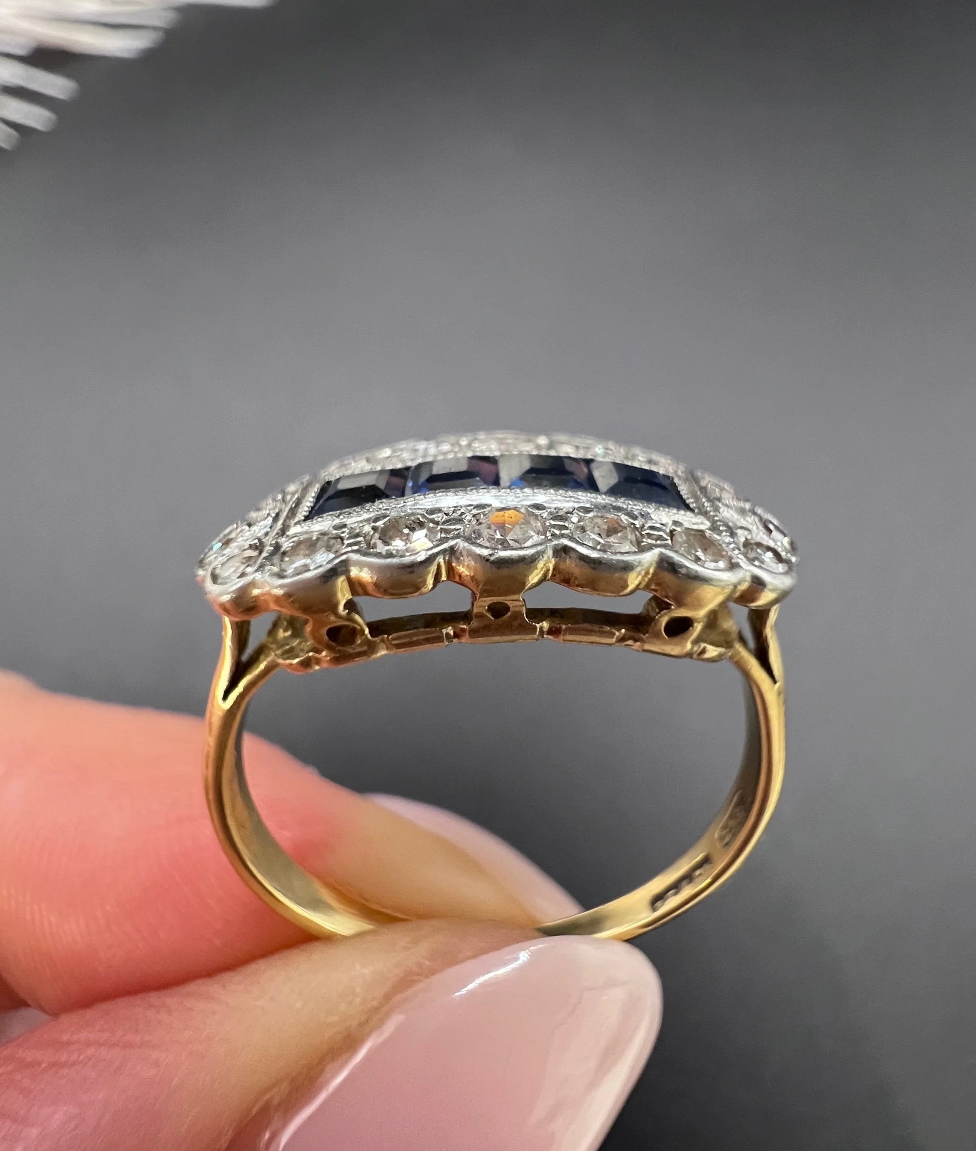 A sapphire and diamond elongated cluster ring in platinum and yellow gold, held in a hand