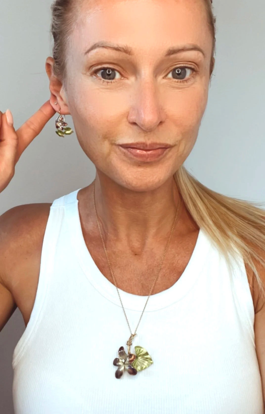 Gold and enamel diamond flower pendant and earring modelled by a lady wearing a white top