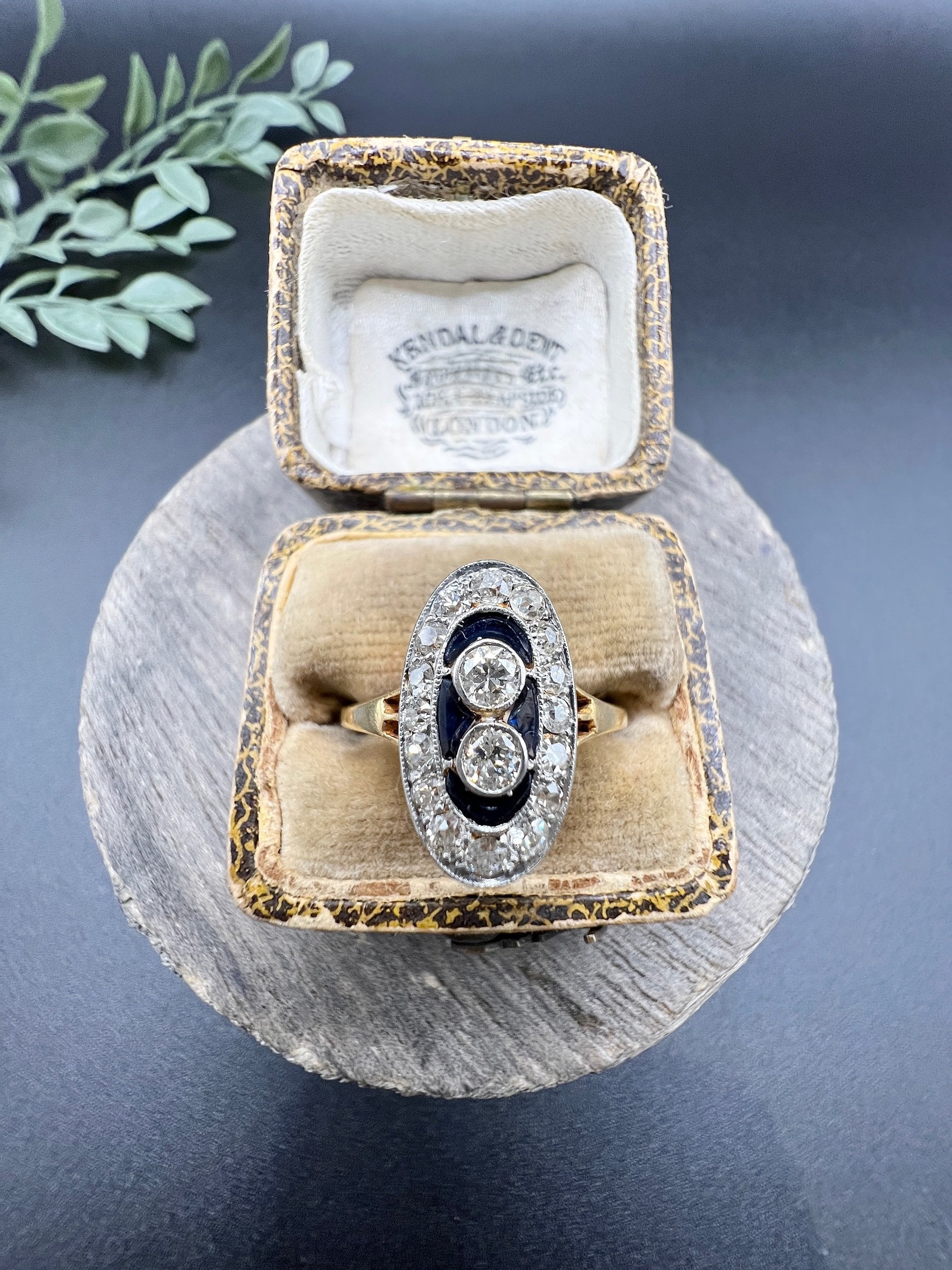 An oval cluster ring with diamonds and sapphires in platinum and yellow gold, in an antique ring box
