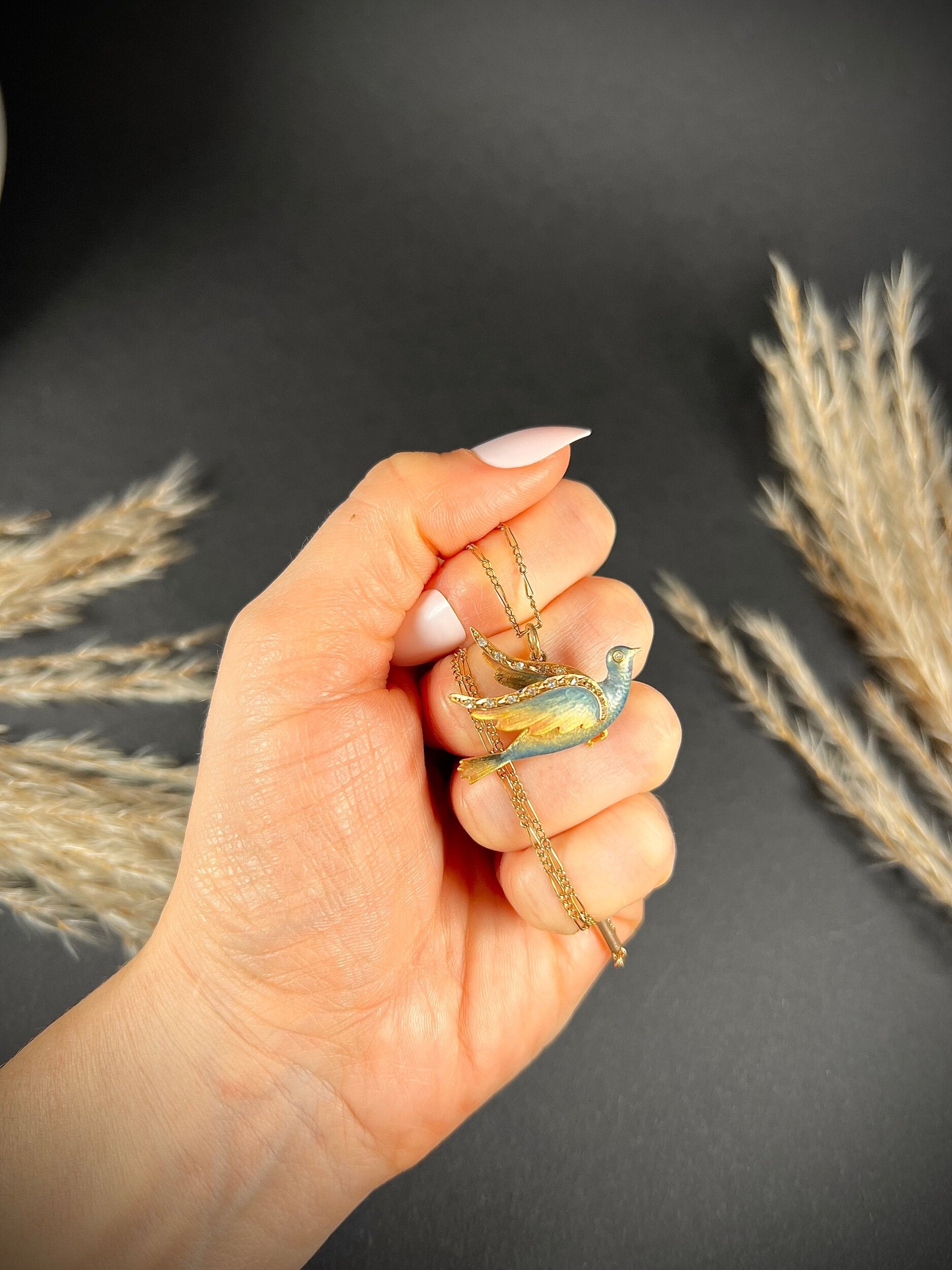 An enamel and diamond dove bird pendant, with a chain, held in a hand