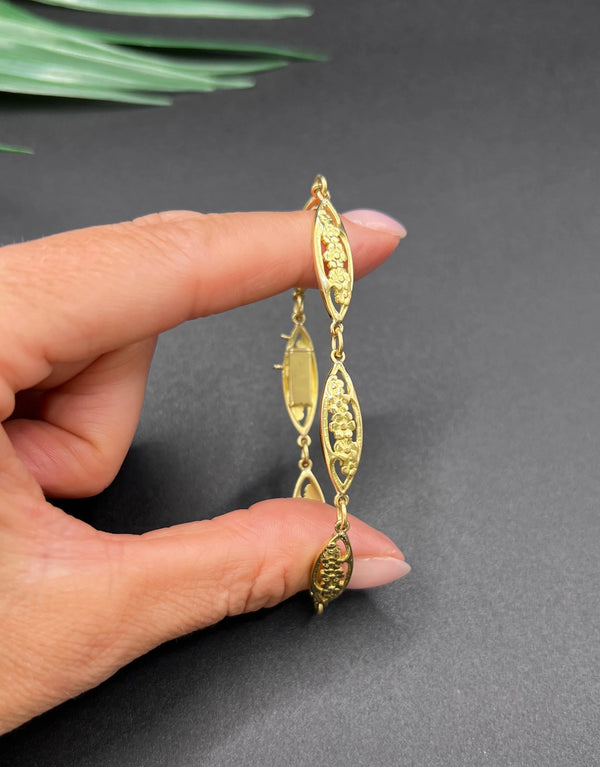 A yellow gold floral link bracelet, held in a hand