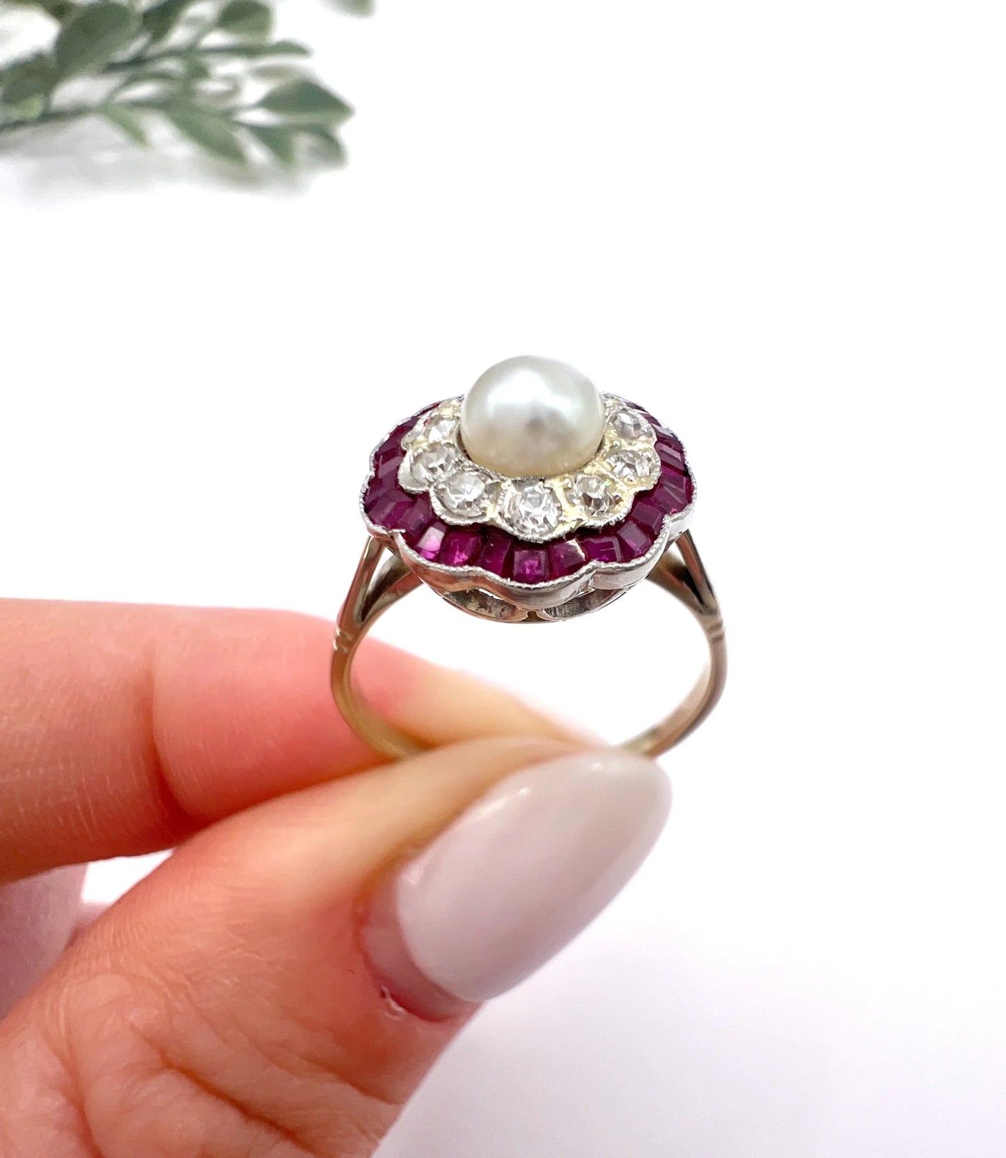 A pearl, diamond and ruby fancy cluster ring in platinum and yellow gold, held in a hand