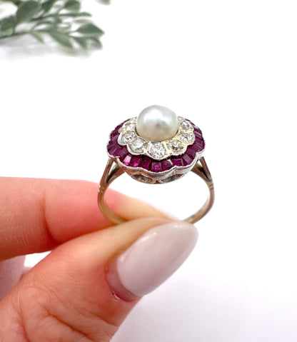 A pearl, diamond and ruby fancy cluster ring in platinum and yellow gold, held in a hand