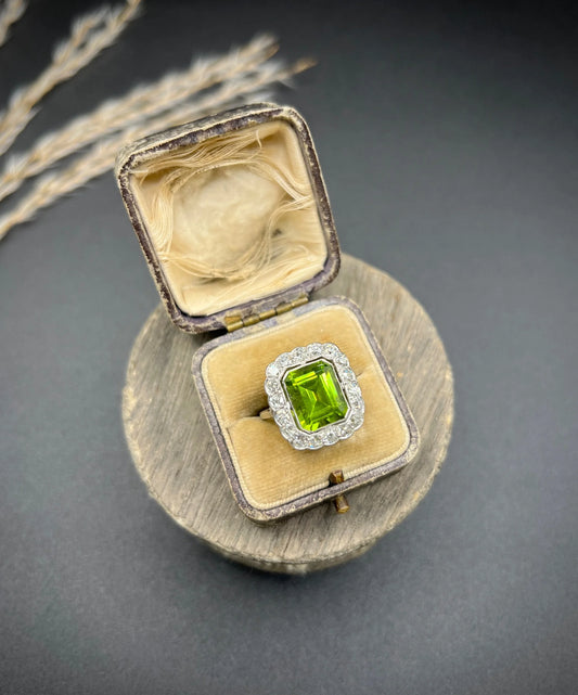A cushion shaped peridot and diamond cluster ring in white metal, in an antique ring box