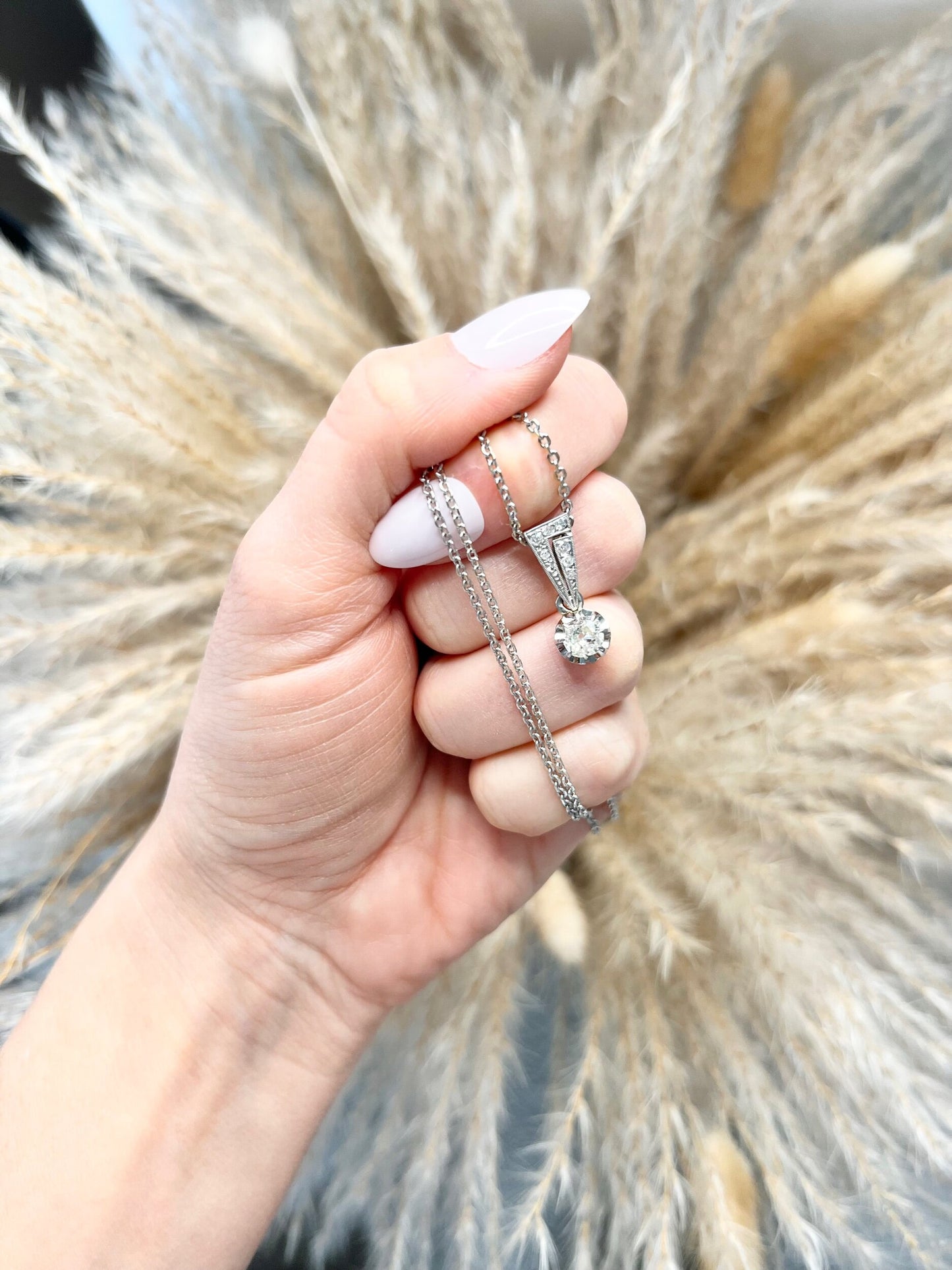 An old cut diamond pendant in white metal with a matching chain, held in a hand