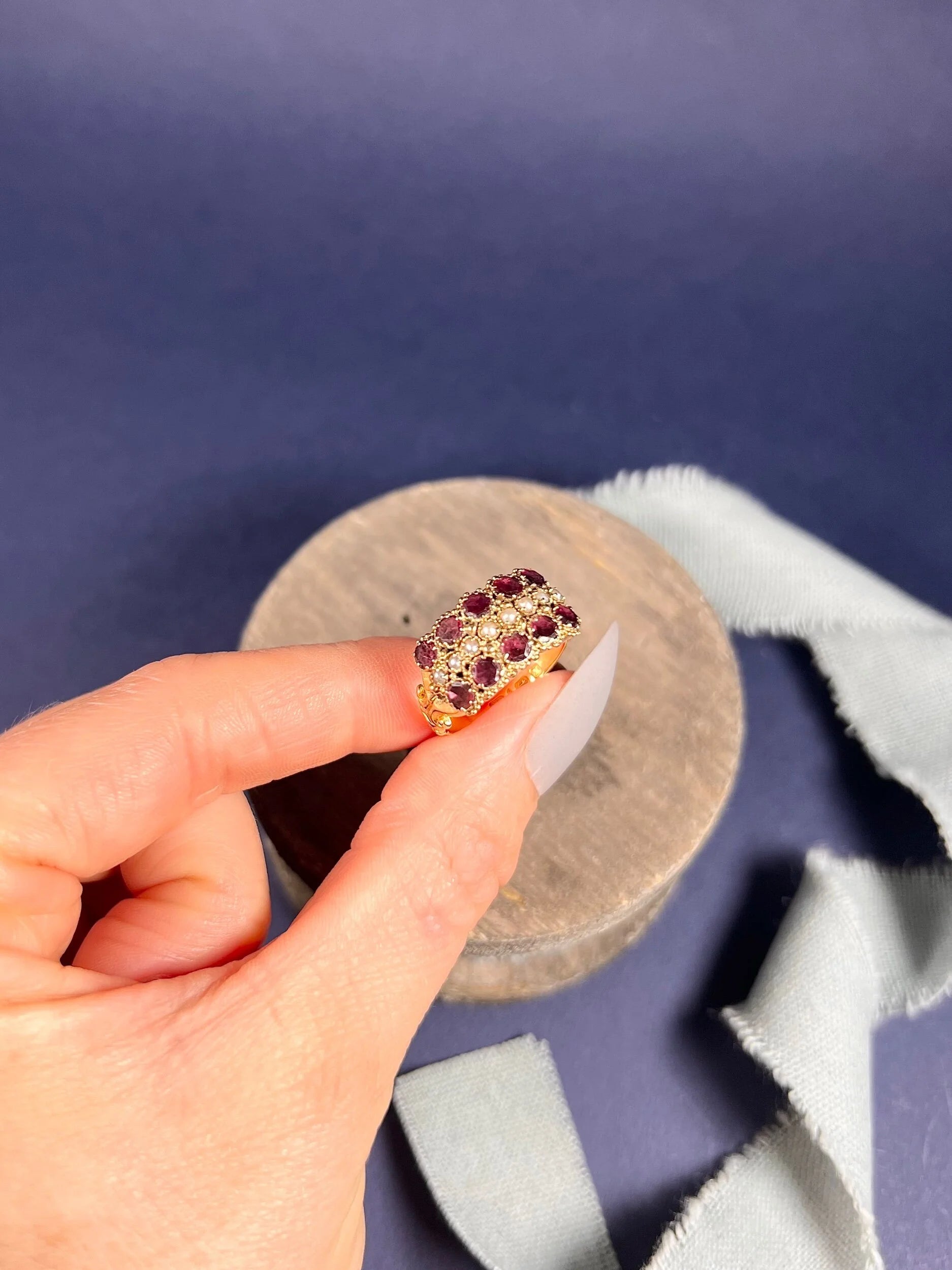 A yellow gold triple row ring with garnets and seed pearls, held in a hand