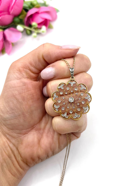 A floral openwork diamond pendant in gold and platinum, with a chain, held in a hand