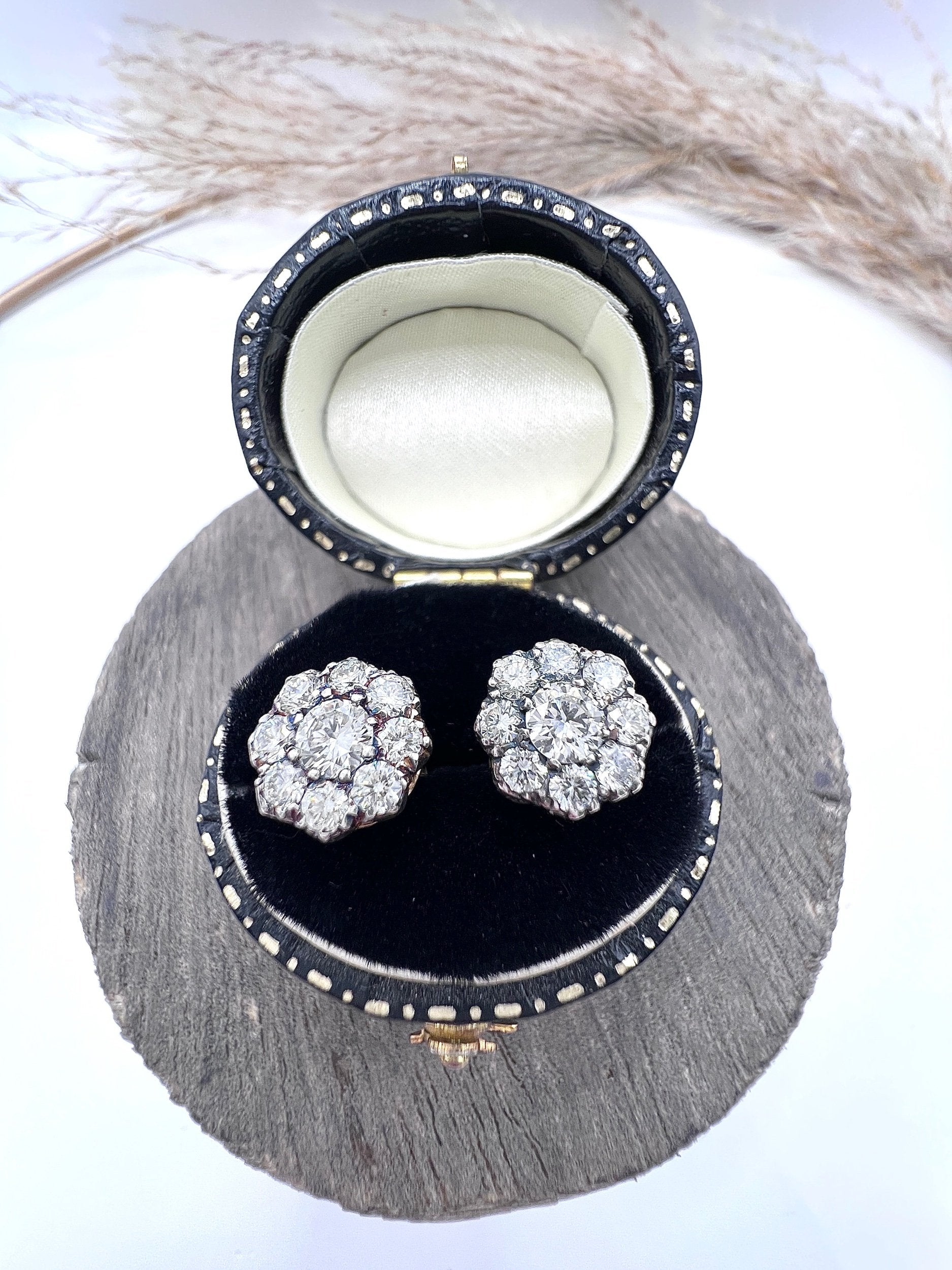 A pair of diamond daisy cluster stud earrings in yellow and white gold, in an earring box