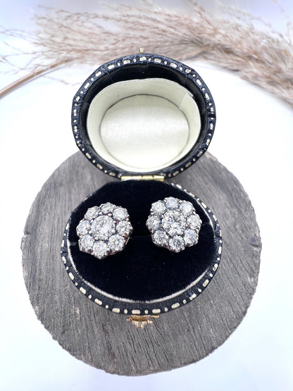 A pair of diamond daisy cluster stud earrings in yellow and white gold, in an earring box