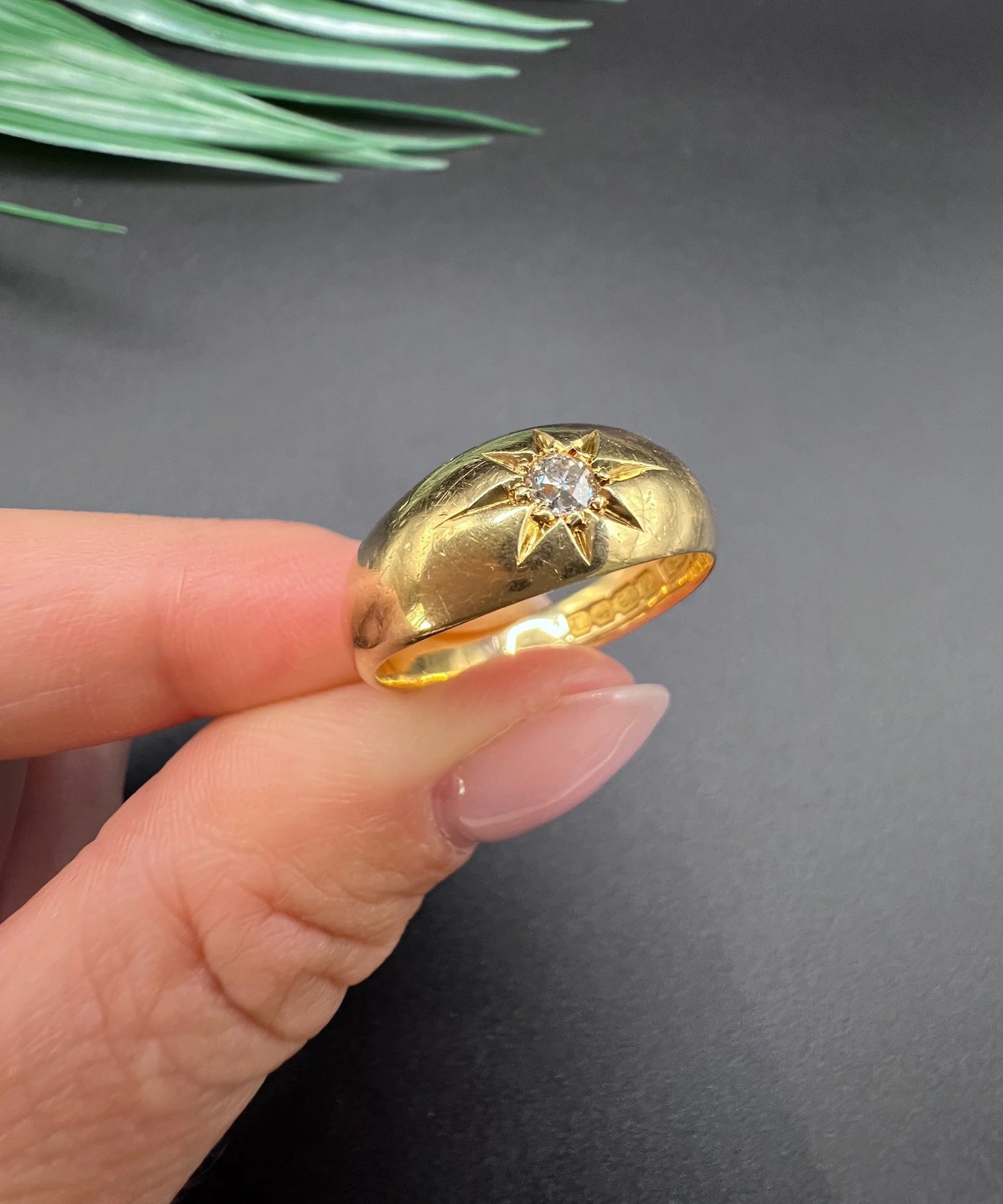A single stone old cut diamond gypsy band ring in yellow gold, held in a hand