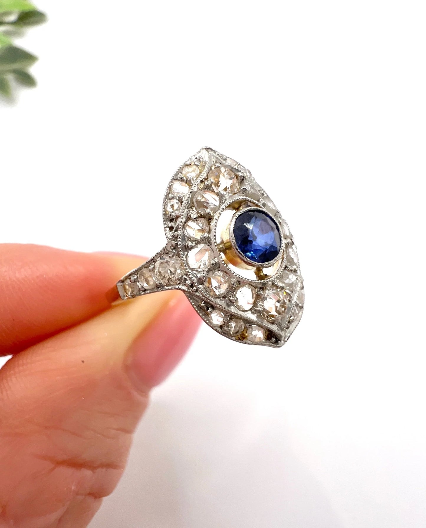 A sapphire and diamond openwork ring in platinum with a yellow gold ring shank, held in a hand