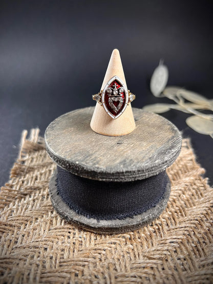 An ornate diamond and enamel navette shaped antique ring, on a ring cone, on top of a wooden spool