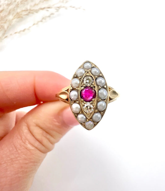 A navette shaped pearl, diamond and ruby cluster ring in yellow gold, held in a hand