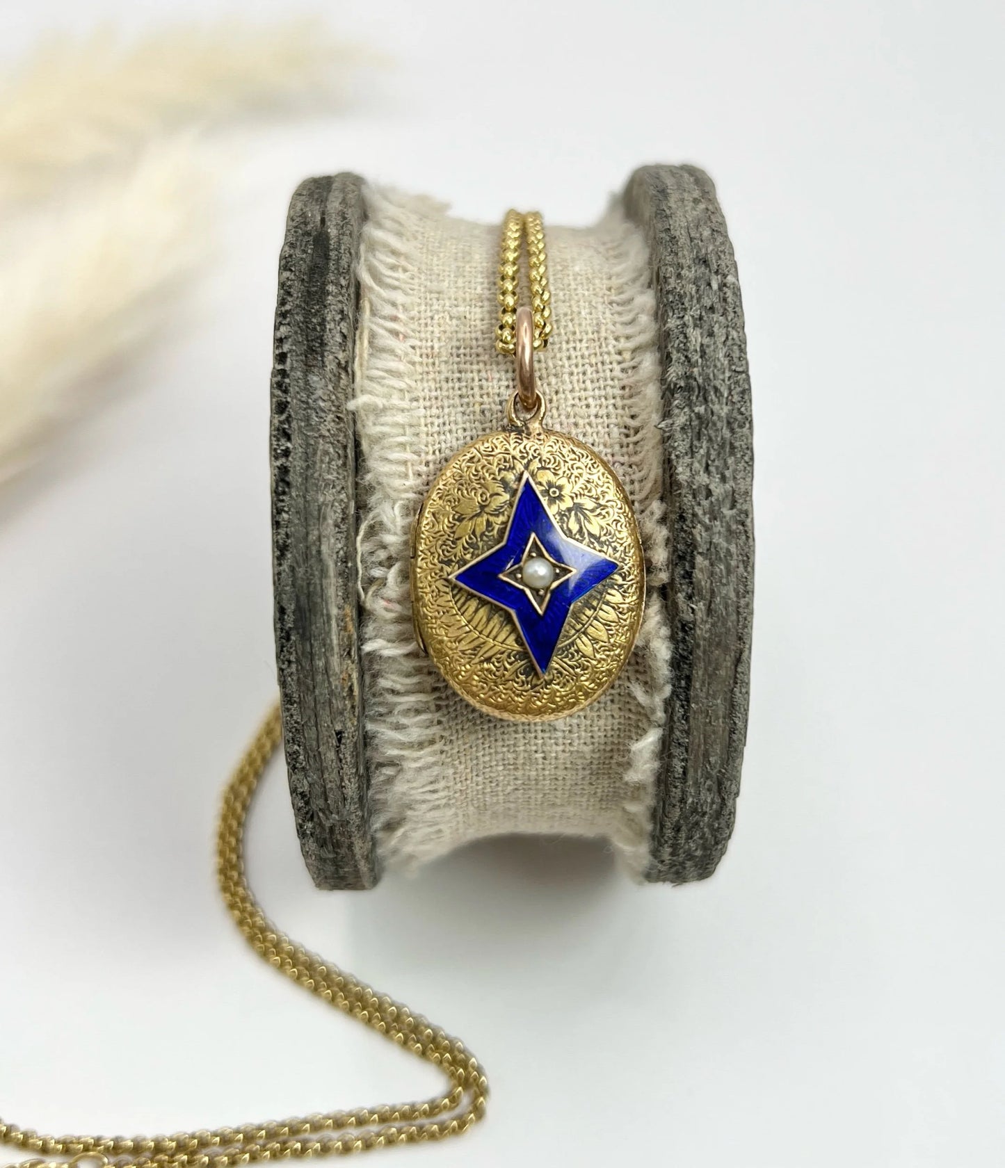 An oval yellow gold locket with a blue enamel star and seed pearl centre, with a chain