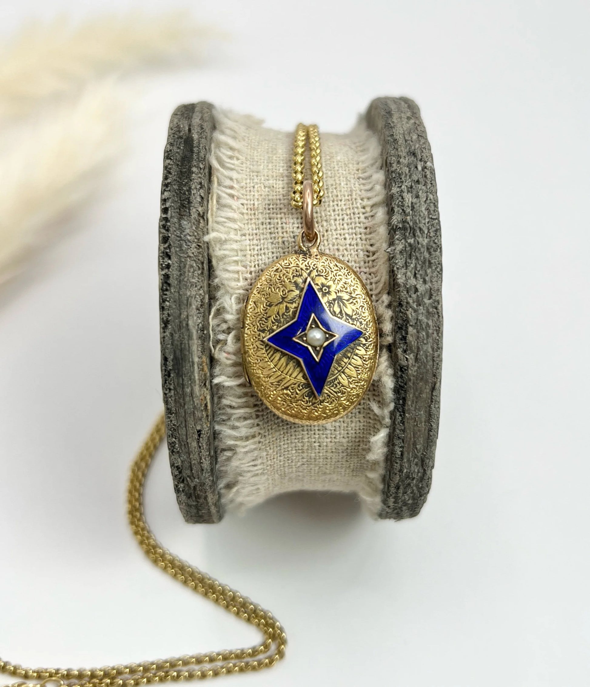 An oval yellow gold locket with a blue enamel star and seed pearl centre, with a chain