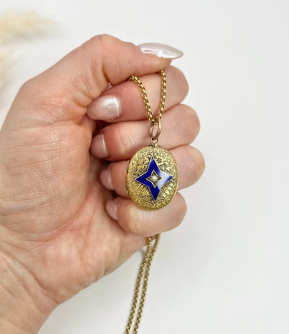 An oval yellow gold locket with a blue enamel star and seed pearl centre, held in a hand, with chain