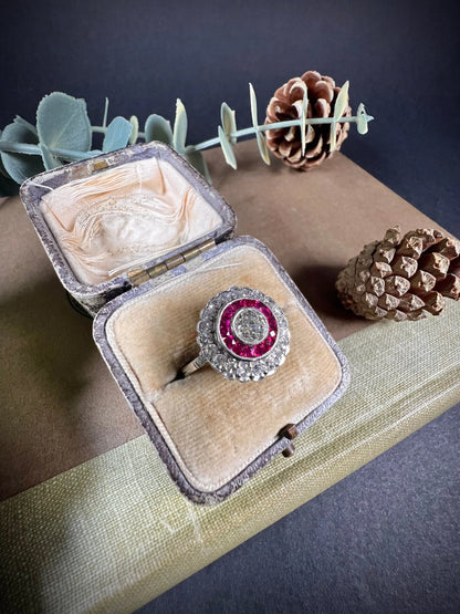 A round cluster ring with rubies and diamonds in white gold, in an antique ring box