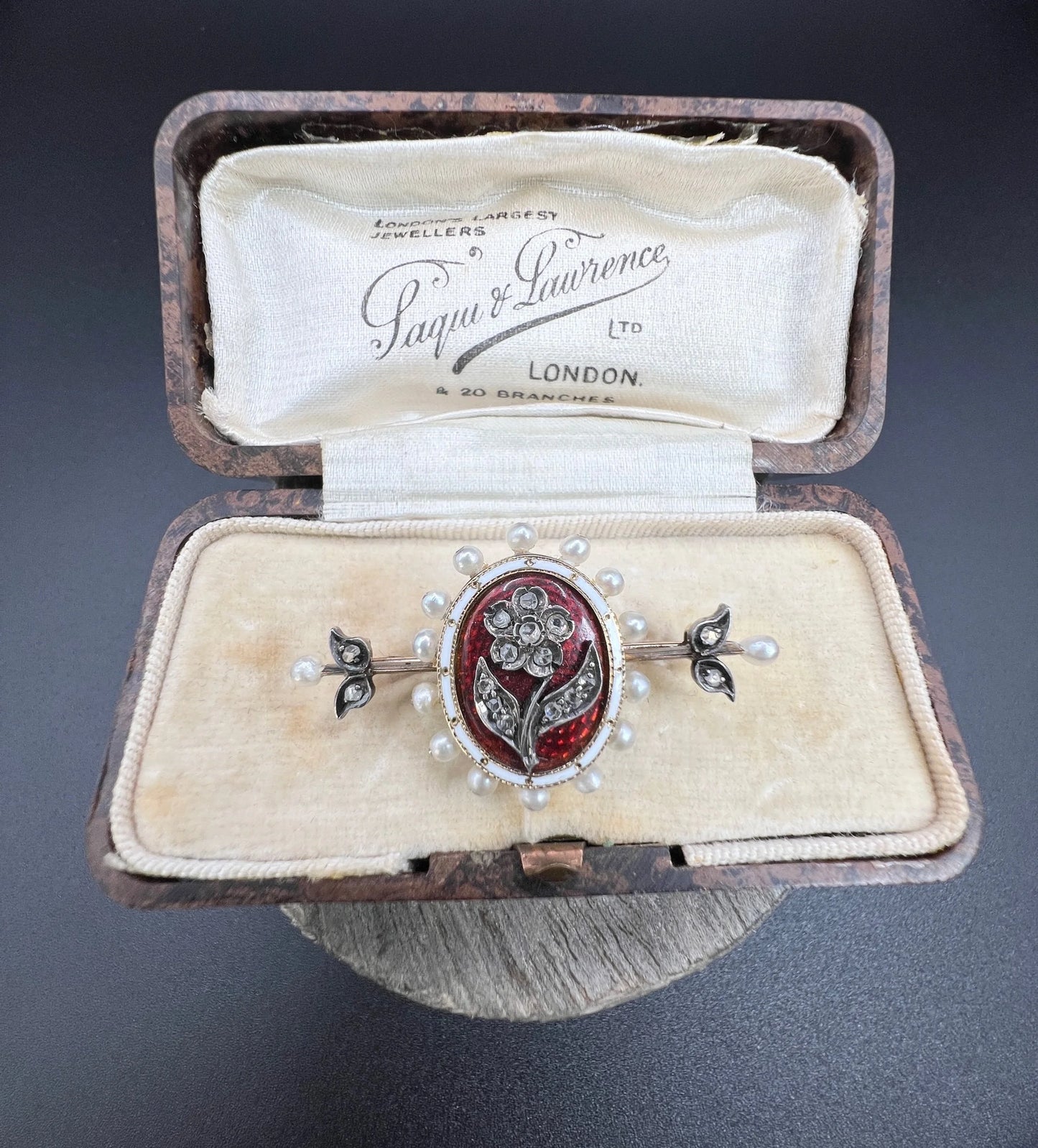 A yellow gold bar brooch with a red enamel centre surrounded by pearls, with a diamond flower motif and diamond leaves at either end, in a box