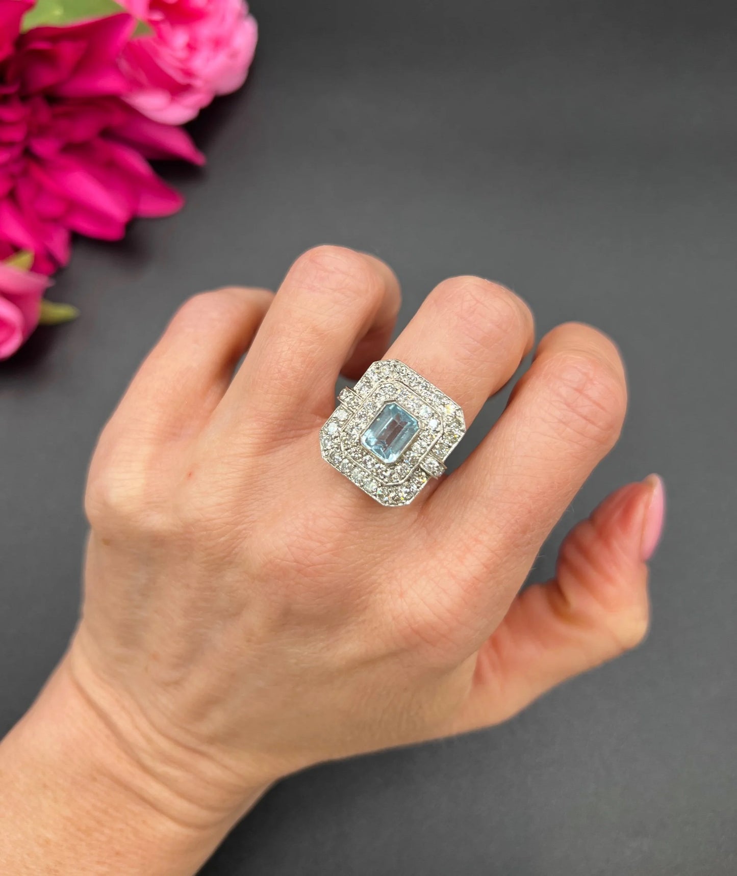 An octagonal shaped cluster ring with an aquamarine centre surrounded by two rows of diamonds, in platinum, modelled on a hand