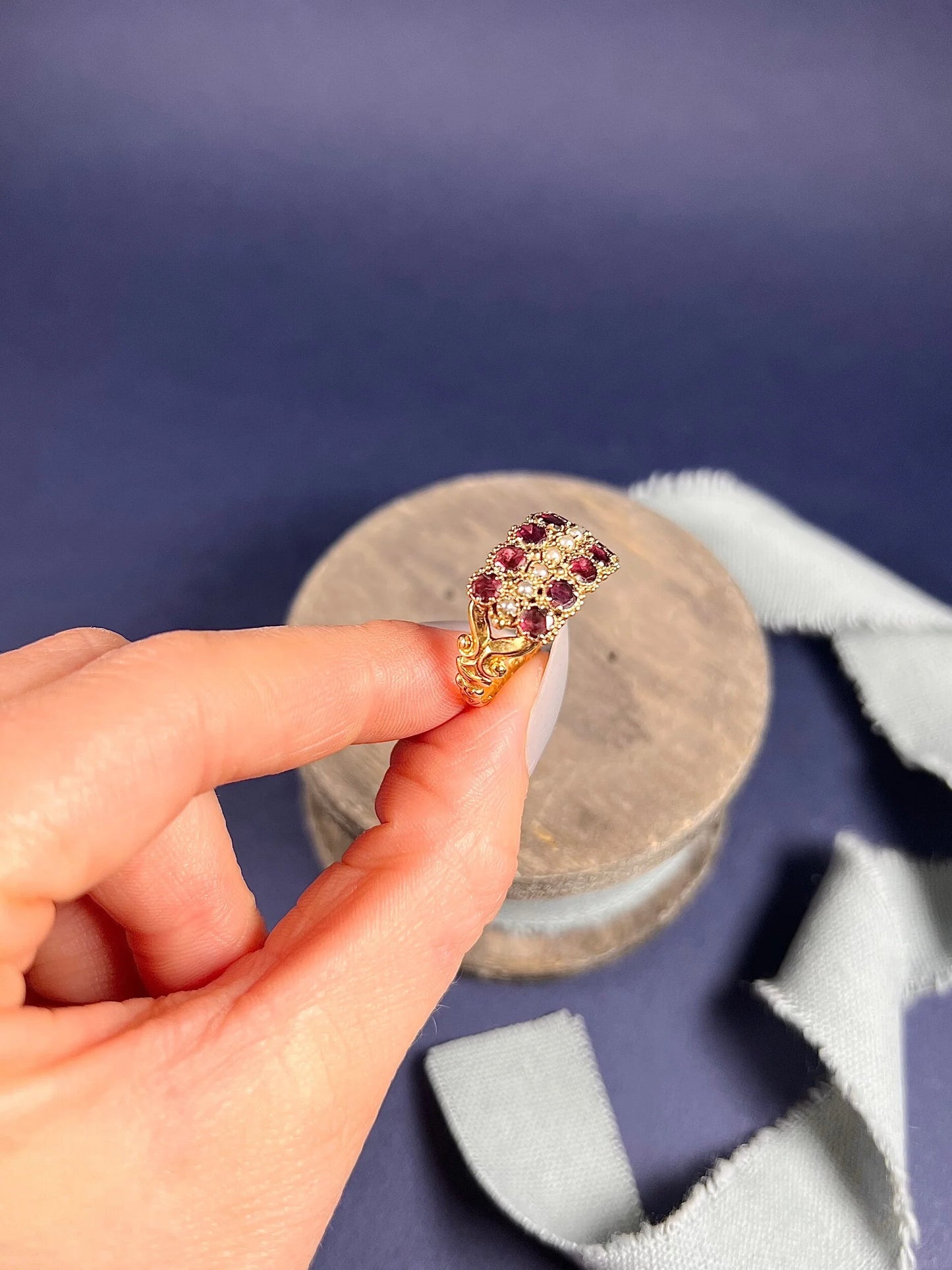A yellow gold triple row ring with garnets and seed pearls, held in a hand