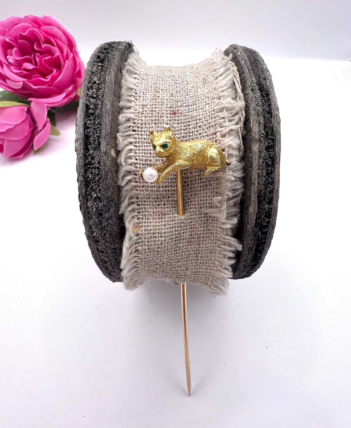 A yellow gold cat playing with a pearl ball stick pin