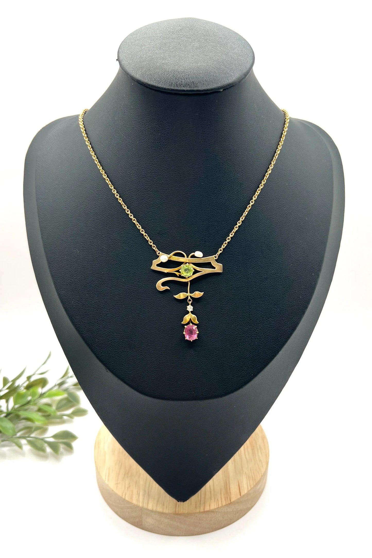 A yellow gold pendant necklace with pearls, a peridot, a diamond and a pink tourmaline drop, on a black jewellery bust