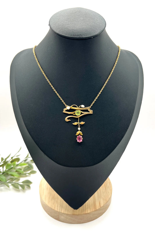 A yellow gold pendant necklace with pearls, a peridot, a diamond and a pink tourmaline drop, on a black jewellery bust