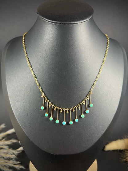 A gold negligee pendant necklace with turquoise drops, on a black bust