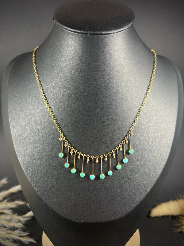 A gold negligee pendant necklace with turquoise drops, on a black bust