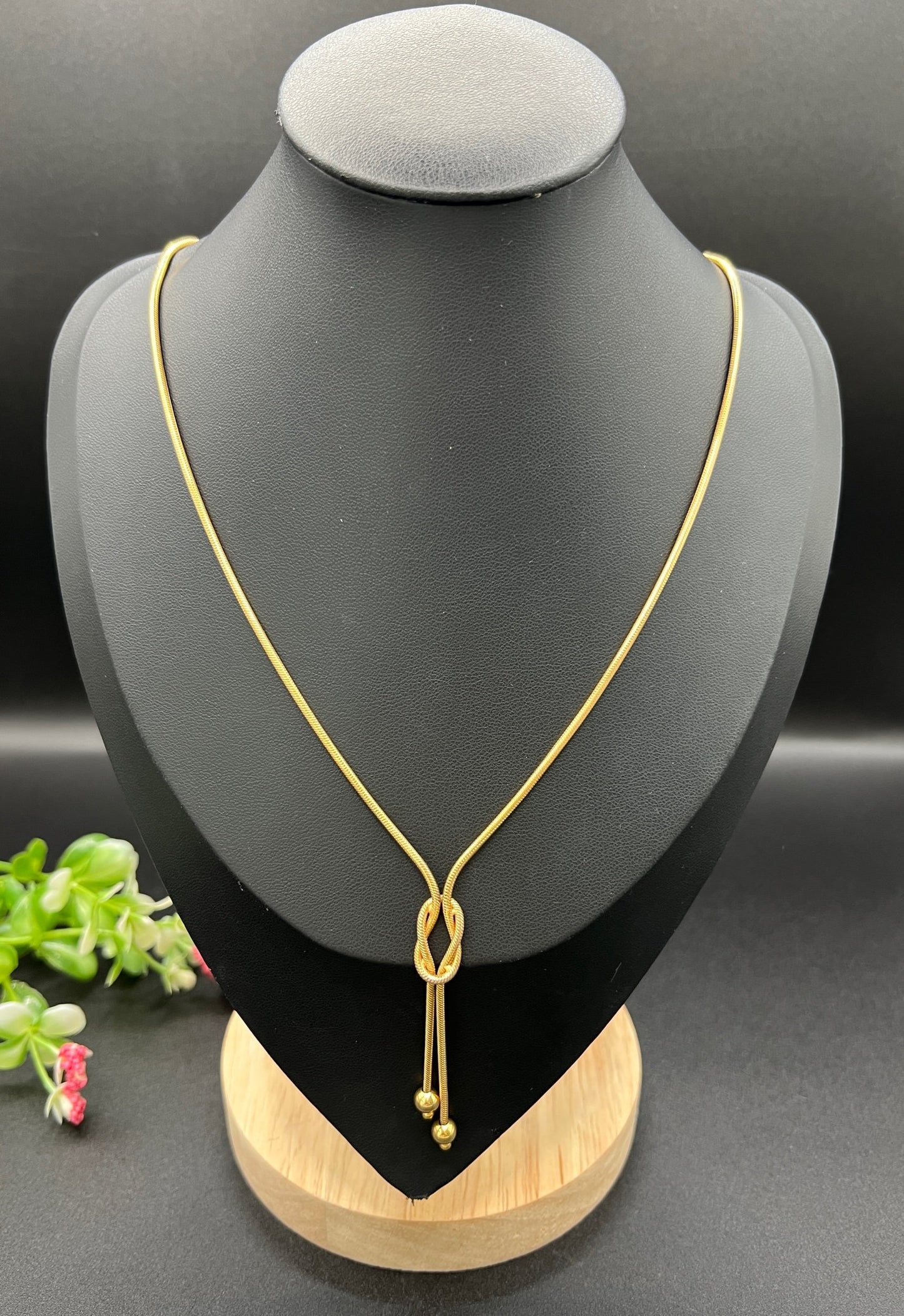 A yellow gold snake link chain necklace with a knot and tassel drop, on a black bust