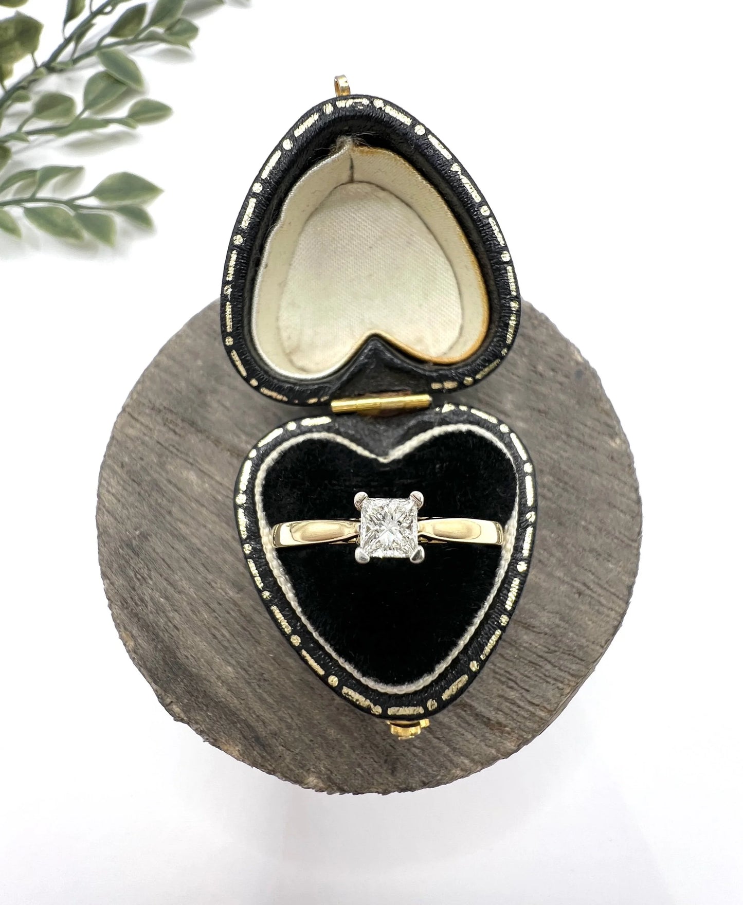 A solitaire princess cut diamond ring in yellow and white gold, in a heart-shaped ring box