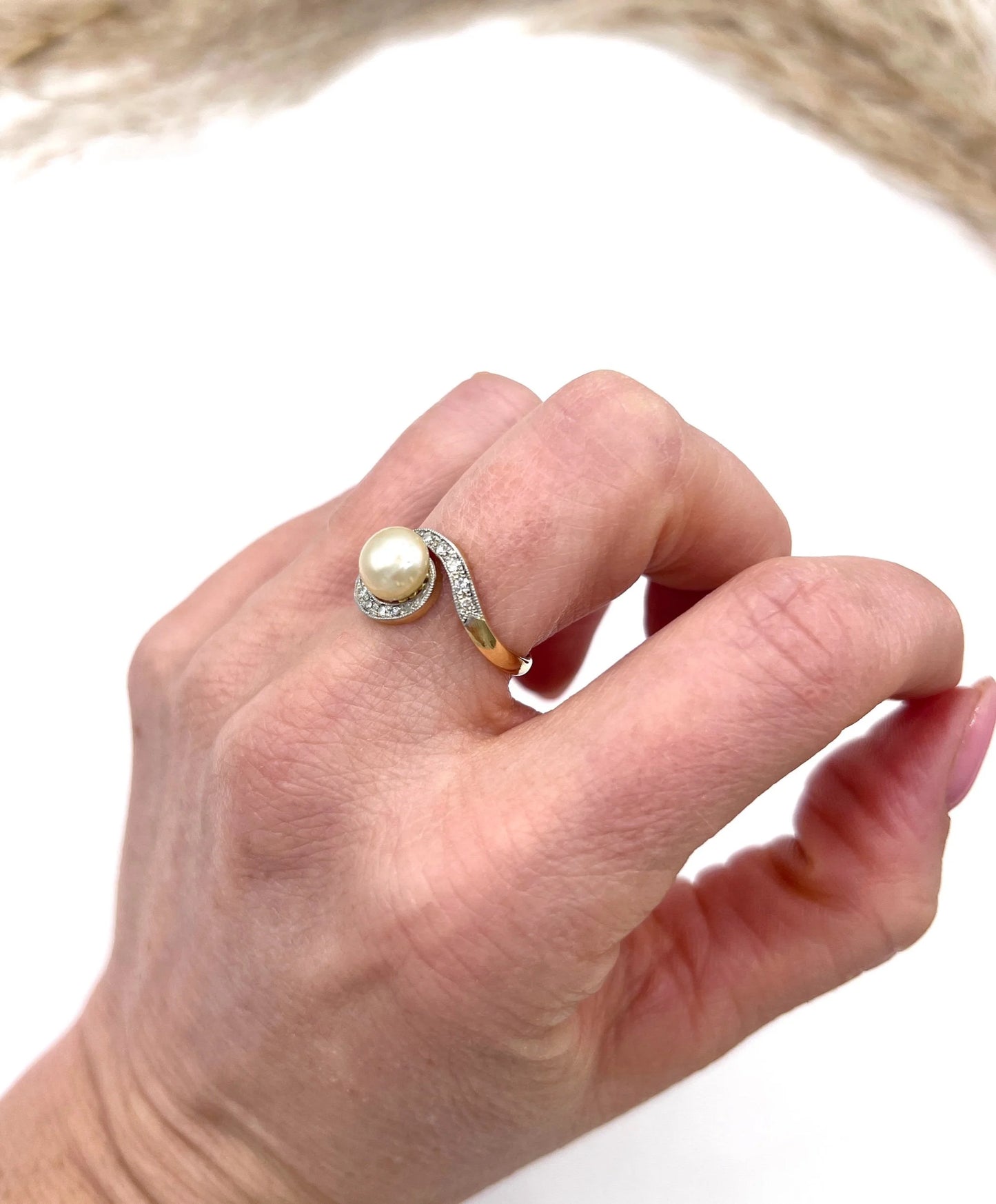 A pearl and diamond crossover swirl ring in yellow and white gold, modelled on a hand