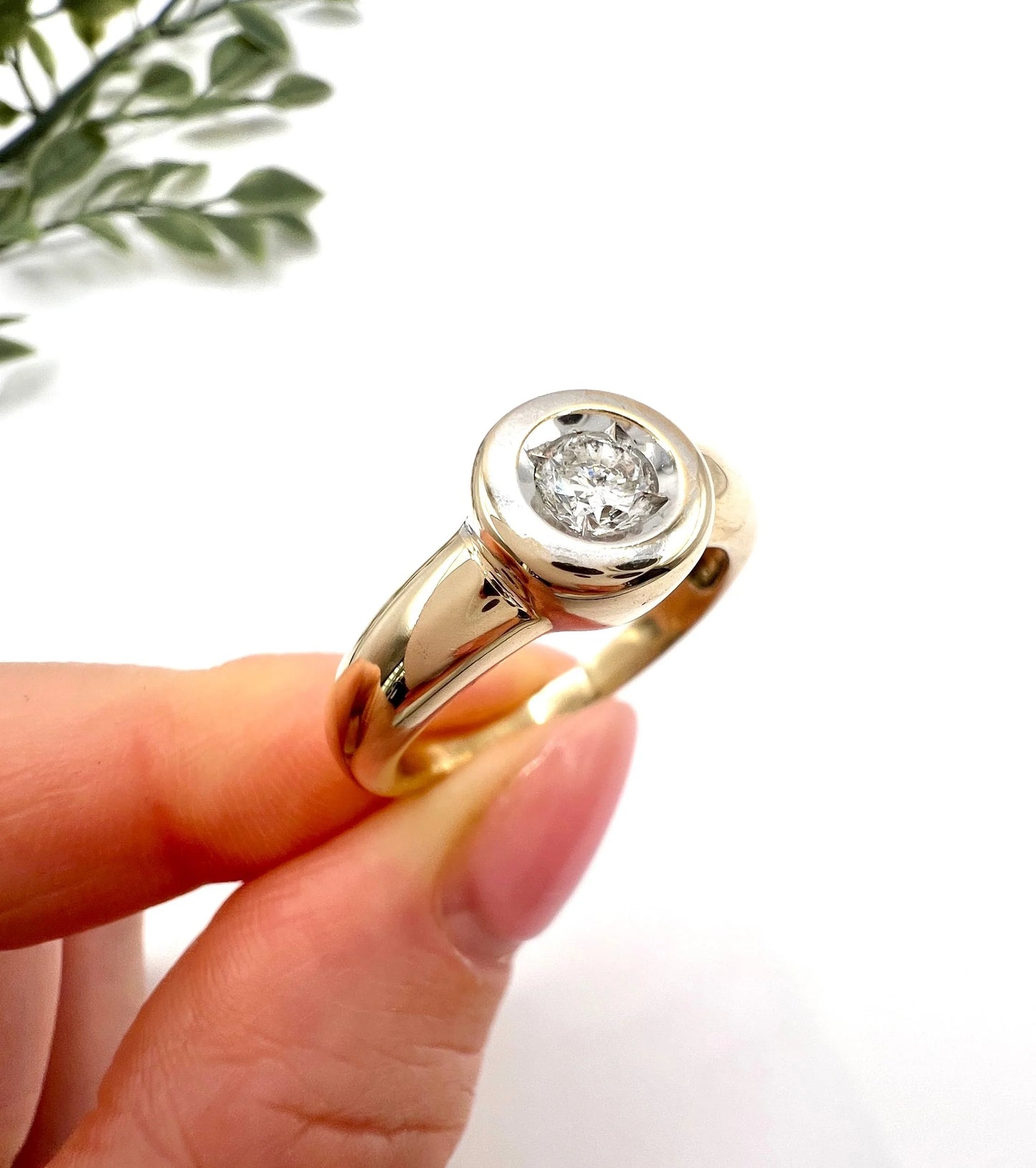 A single stone brilliant cut diamond ring bezel set in yellow gold, held in a hand